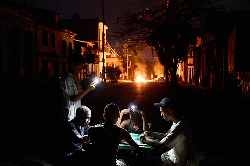 People illuminate themselves with their phones while playing dominoes during a power outage in Havana, 14 May, 2026
