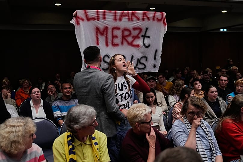 Eine junge Frau protestiert während einer Rede von Bundeskanzler Friedrich Merz bei einer Diskussion auf dem Deutschen Katholikentag am 15. Mai 2026 in Würzburg.