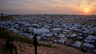 شباب فلسطينيون ينظرون وهم يقفون في منطقة بجوار الخيام في مخيم مؤقت للنازحين، عند غروب الشمس في خان يونس، جنوب قطاع غزة، الخميس 9 أبريل 2026. 