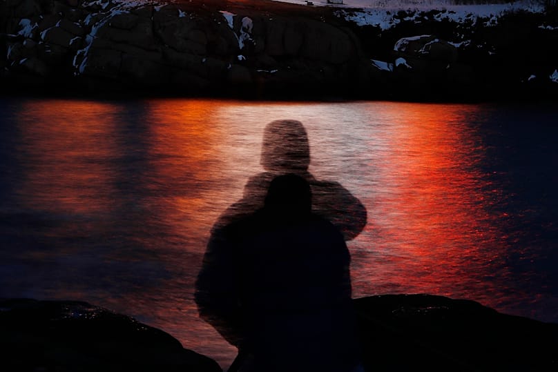 Nesta fotografia tirada com exposição prolongada, vê-se a silhueta de um homem contra as luzes refletidas nas águas ao largo do Cabo Neddick, no Maine. 11.12.2017