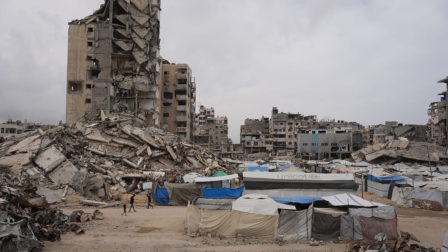 Palestinianos caminham por uma rua rodeada de edifícios destruídos durante a guerra entre Israel e o Hamas, na cidade de Gaza, sexta-feira, 15 de maio de 2026.