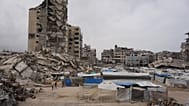 Palestinianos caminham por uma rua rodeada de edifícios destruídos durante a guerra entre Israel e o Hamas, na cidade de Gaza, sexta-feira, 15 de maio de 2026.