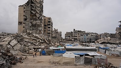 Des Palestiniens marchent dans une rue bordée de bâtiments détruits pendant la guerre entre Israël et le Hamas, à Gaza, le vendredi 15 mai 2026. 