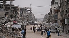 فلسطينيون يسيرون في شارع محاط بمبانٍ دمرت خلال حرب حماس الإسرائيلية، في مدينة غزة، الجمعة 15 مايو/أيار 2026. (صورة من وكالة أسوشييتد برس/عبد الكريم حنا)
