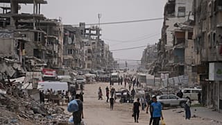فلسطينيون يسيرون في شارع محاط بمبانٍ دمرت خلال حرب حماس الإسرائيلية، في مدينة غزة، الجمعة 15 مايو/أيار 2026. (صورة من وكالة أسوشييتد برس/عبد الكريم حنا)
