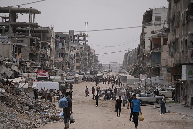 Palestinians walk along a street surrounded by buildings destroyed during the Israel Hamas war in Gaza City, 15 May, 2026