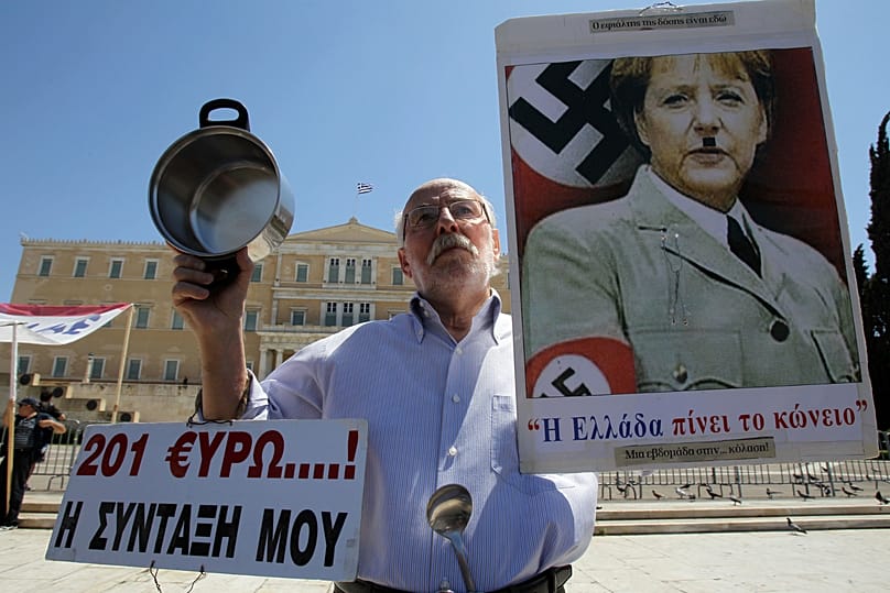 An elderly man holds a poster with a picture of German Chancellor Angela Merkel, made to look like Adolf Hitler during a protest in Athens. May 1, 2013 (AP Photo/Thanassis) 