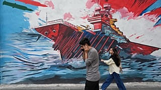 Passanti davanti a un murales comparso a Teheran raffigurante un portaerei Usa sotto attacco di missili