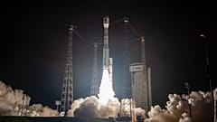 Nachtaufnahme der Vega-C-Rakete mit der SMILE-Mission auf der Startrampe, umgeben von vier Metallpylonen und dichten Rauchschwaden.