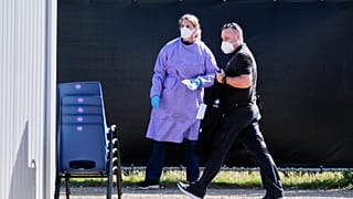 Un miembro de la tripulación pasa junto a una mujer con ropa protectora tras desembarcar del crucero MV Hondius al llegar al puerto de Rotterdam, Países Bajos, 18 mayo 2026 