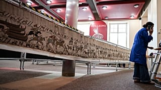 Eine Mitarbeiterin blickt auf ihr Handy, bevor sie am achtzehnten September zweitausendfünfundzwanzig in Bayeux den Bayeux-Teppich fürs British Museum verpackt.