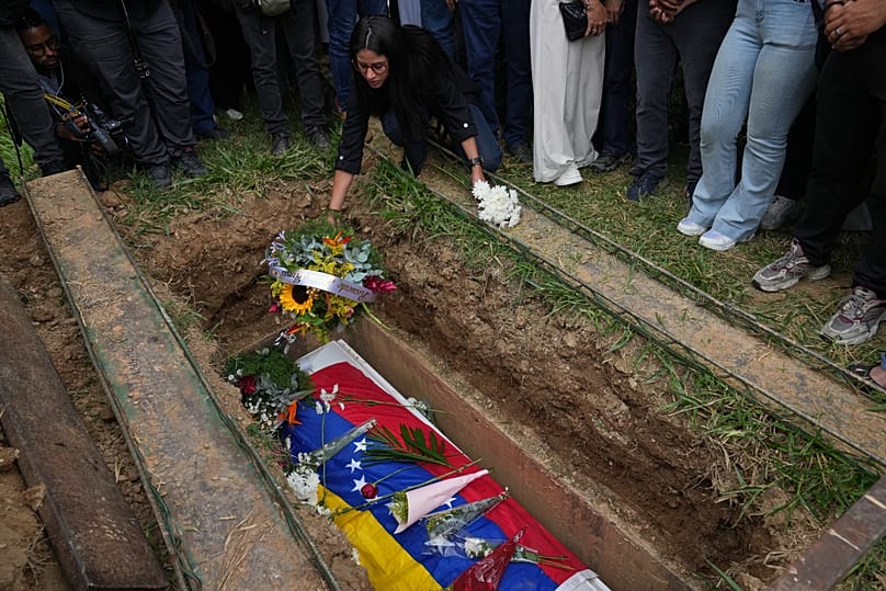 Una amiga deposita flores sobre el ataúd de Carmen Navas, madre de Víctor Hugo Quero, quien falleció bajo custodia tras su arresto casi un año antes, 19 de mayo de 2026.