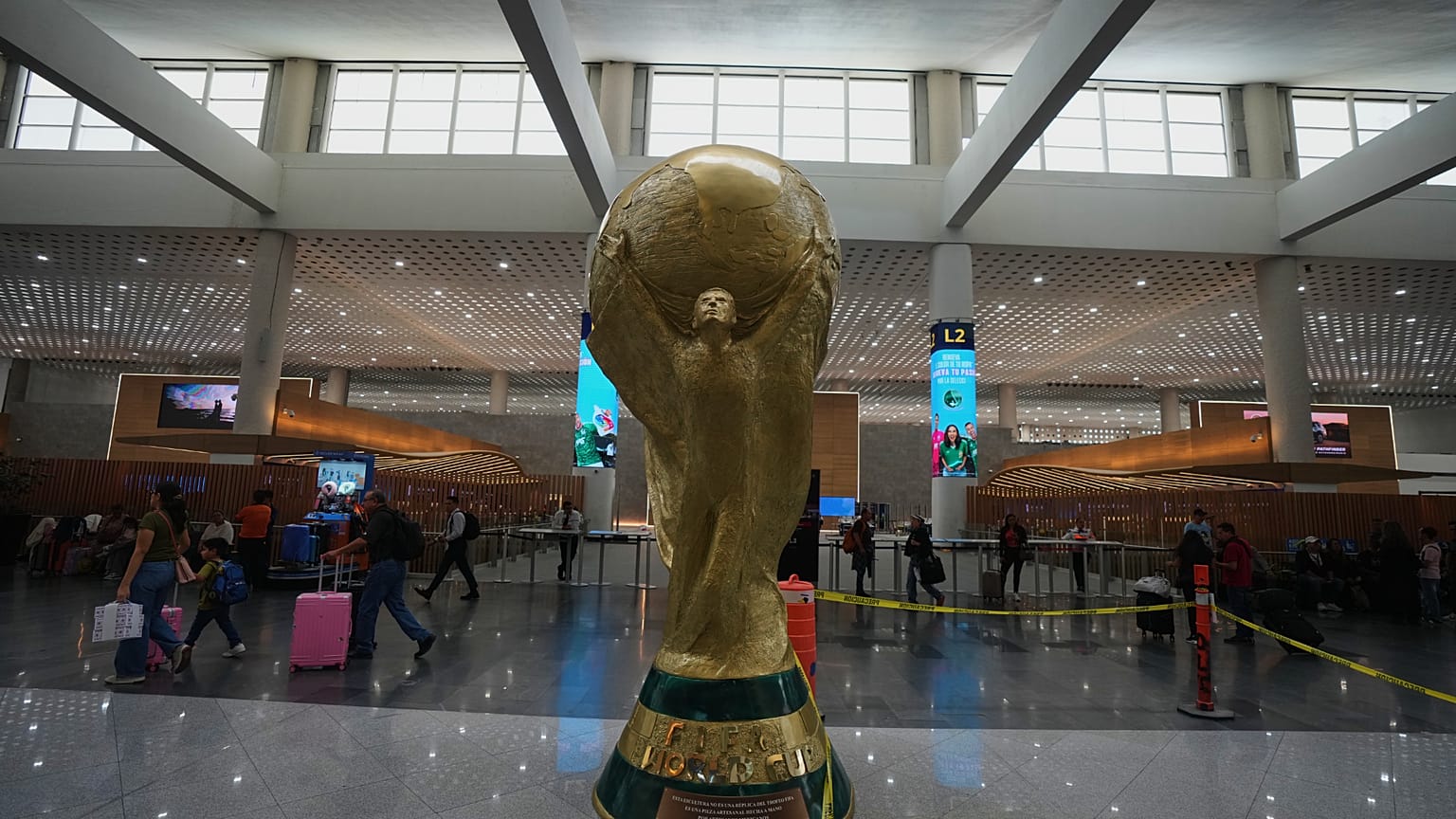 Pasajeros caminan junto a una escultura del trofeo de la Copa Mundial en el Aeropuerto Internacional Benito Juárez, en Ciudad de México, el martes 19 de mayo de 2026.