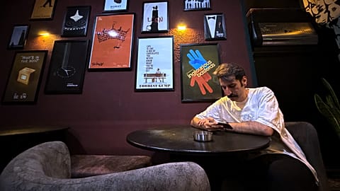 A man looks at his smart phone as he sits under posters of Hollywood movies at a cafe in Tehran, 8 May 2026