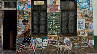 A woman wearing U.S. flag motif pants walks past a building that houses an art installation on the Cuban Revolution