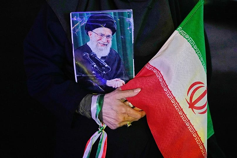 A demonstrator holds a poster of late Ayatollah Ali Khamenei and an Iranian flag during a pro-government gathering at a square in downtown Tehran, Iran, 19 May 2026