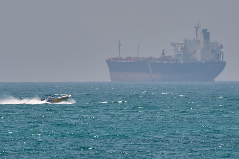 FILE: A boat sails past a tanker anchored on the Strait of Hormuz off the coast Qeshm island, Iran, 18 April 2026.