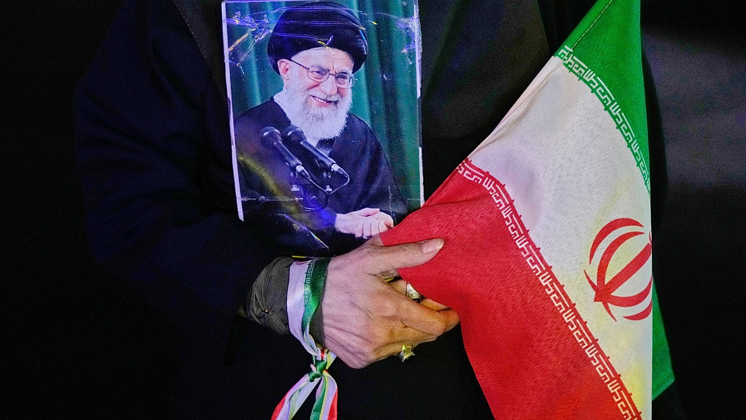 متظاهر يحمل ملصقًا للمرشد الأعلى الإيراني المقتول آية الله علي خامنئي، الذي قُتل في الغارة الأمريكية والإسرائيلية في 28 فبراير، وعلمًا إيرانيًا خلال تجمع مؤيد للحكومة
