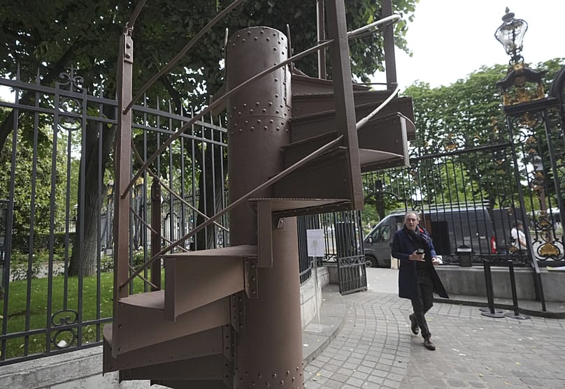 Egy férfi elhalad az Eiffel-torony eredeti, 1889-ből származó csigalépcsőjének egy darabja előtt a párizsi Artcurial aukciósházban 2026. május 13-án, szerdán