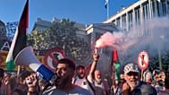 Manifestante ergue um sinal de fumo enquanto outros entoam palavras de ordem pró-palestinianas