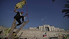 أحد مؤيدي حزب الله يلتقط صورة سيلفي وهو يلوح بعلم حزب الله بينما يقف على شجرة خارج السفارة الإيرانية في بيروت، لبنان