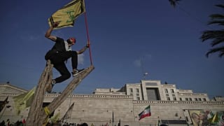 أحد مؤيدي حزب الله يلتقط صورة سيلفي وهو يلوح بعلم حزب الله بينما يقف على شجرة خارج السفارة الإيرانية في بيروت، لبنان