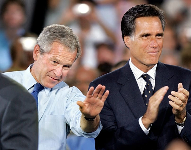 O presidente dos EUA, George W. Bush, acena enquanto o governador do Massachusetts, Mitt Romney, aplaude num comício em Nashua, New Hampshire, a 30 de agosto de 2004  (AP Photo/Steven Senne, File)