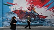 People walk past a mural depicting a U.S. aircraft carrier under missile attack in downtown Tehran, Iran, Sunday, May 17, 2026.