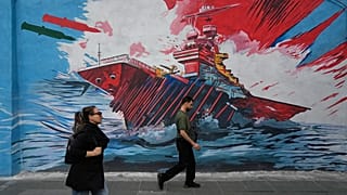 People walk past a mural depicting a U.S. aircraft carrier under missile attack in downtown Tehran, Iran, Sunday, May 17, 2026.