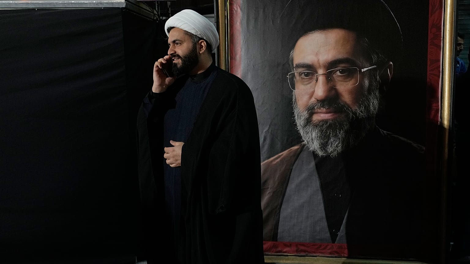 رجل دين يتحدث عبر هاتفه المحمول إلى جانب صورة للمرشد الأعلى الإيراني مجتبى خامنئي، طهران، إيران، الاثنين 18 مايو/أيار 2026. 