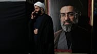 رجل دين يتحدث عبر هاتفه المحمول إلى جانب صورة للمرشد الأعلى الإيراني مجتبى خامنئي، طهران، إيران، الاثنين 18 مايو/أيار 2026. 