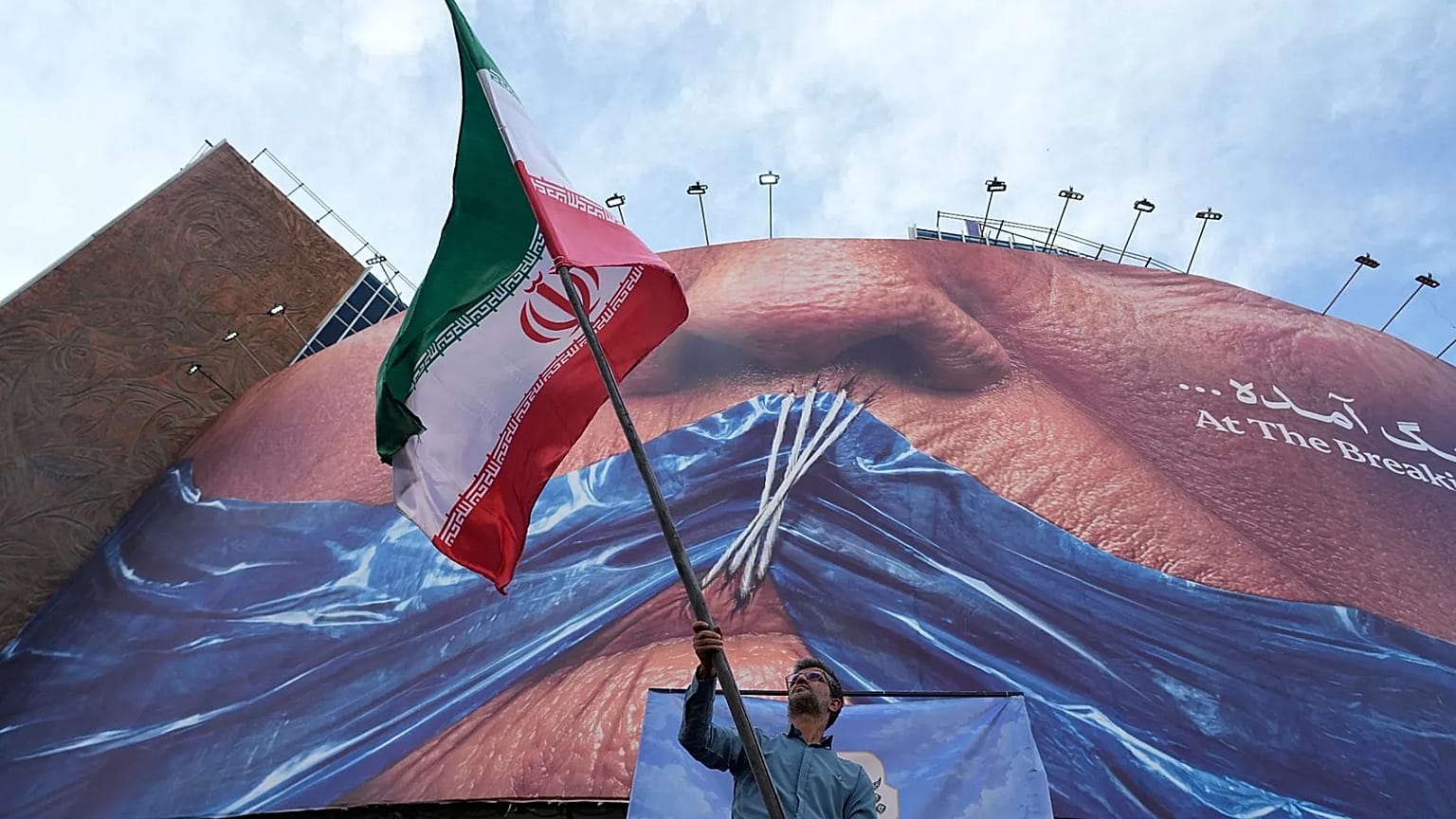 A man waves an Iranian flag under a billboard of the Strait of Hormuz and the sewn lips of US President Donald Trump in Tehran, 6 May, 2026