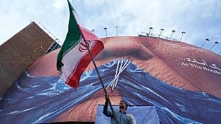A man waves an Iranian flag under a billboard of the Strait of Hormuz and the sewn lips of US President Donald Trump in Tehran, 6 May, 2026