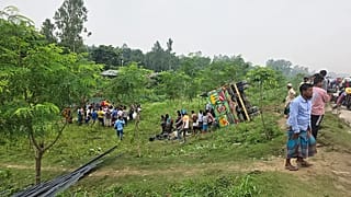 Des passants observent un camion transportant des barres de fer et des passagers en surnombre renversé sur une autoroute du district central de Tangail, le 25 mai 2026