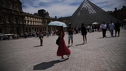 FILE- A woman holds her umbrella to protect from the sun at the Louvre Museum as the temperature rose up to 31 degrees Celsius  in Paris on Friday, June 20, 2025
