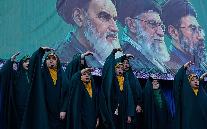 Girls sing a song as they show the movement of missiles with their hands next to the portraits of the late Iranian revolutionary founder Ayatollah Khomeini, left, late Supreme