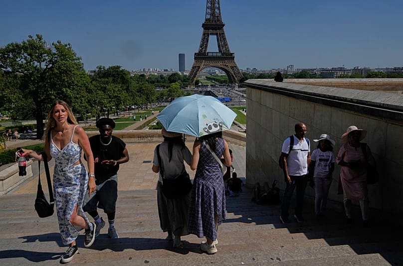 Turisti al riparo di ombrelli per ripararsi dal sole nei pressi della Torre Eiffel (26 maggio 2026)