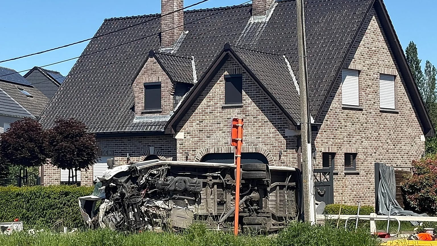 Um veículo jaz de lado junto a uma casa após uma colisão entre um comboio e uma carrinha numa passagem de nível em Buggenhout, Bélgica, terça-feira, 26 de maio de 2026.