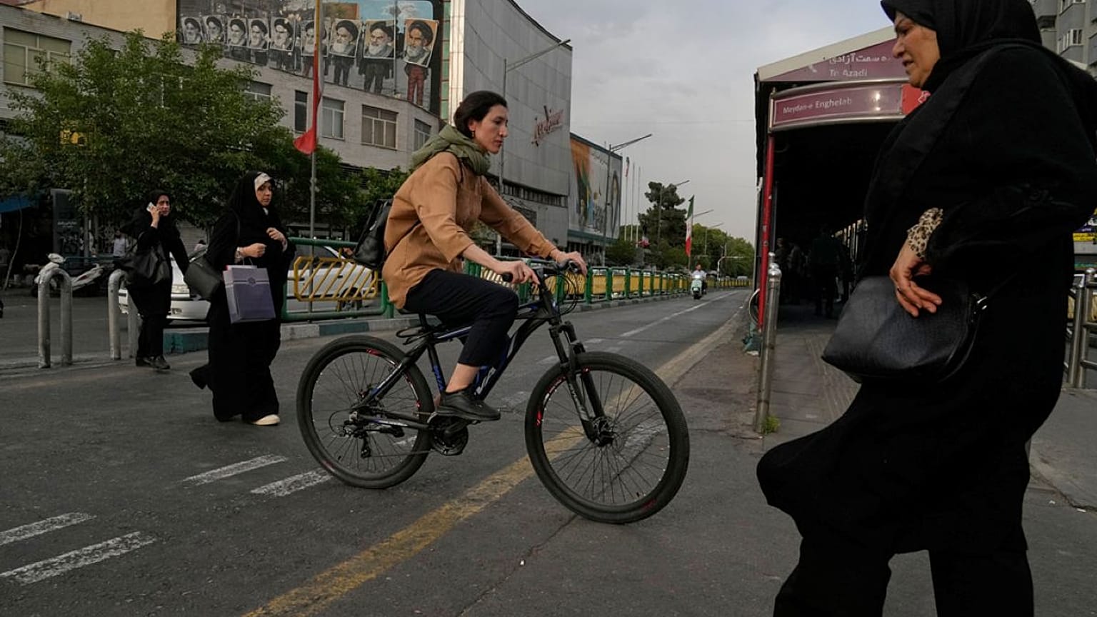  امرأة تقود دراجة هوائية بينما يعبر آخرون شارعاً في وسط مدينة طهران، إيران، الأحد 24 مايو/أيار 2026.