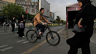  امرأة تقود دراجة هوائية بينما يعبر آخرون شارعاً في وسط مدينة طهران، إيران، الأحد 24 مايو/أيار 2026.