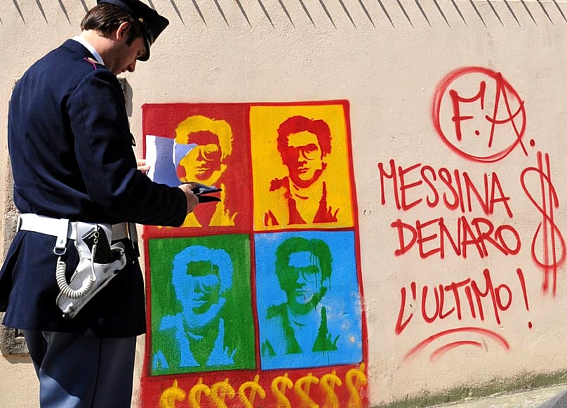An Italian Police officer looks on at graffiti on the perimeter wall of Palermo's city's cathedral portraying Matteo Messina Denaro, 24 April, 2008