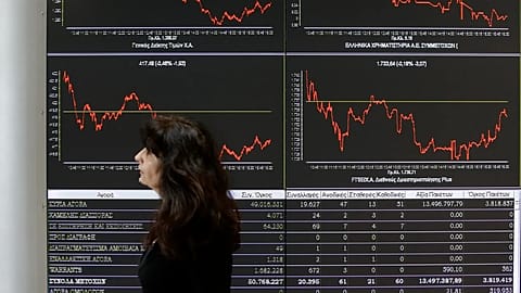 An employee of the Stock Exchange passes a display showing stock price movements in Athens, Wednesday, April 9, 2014. 