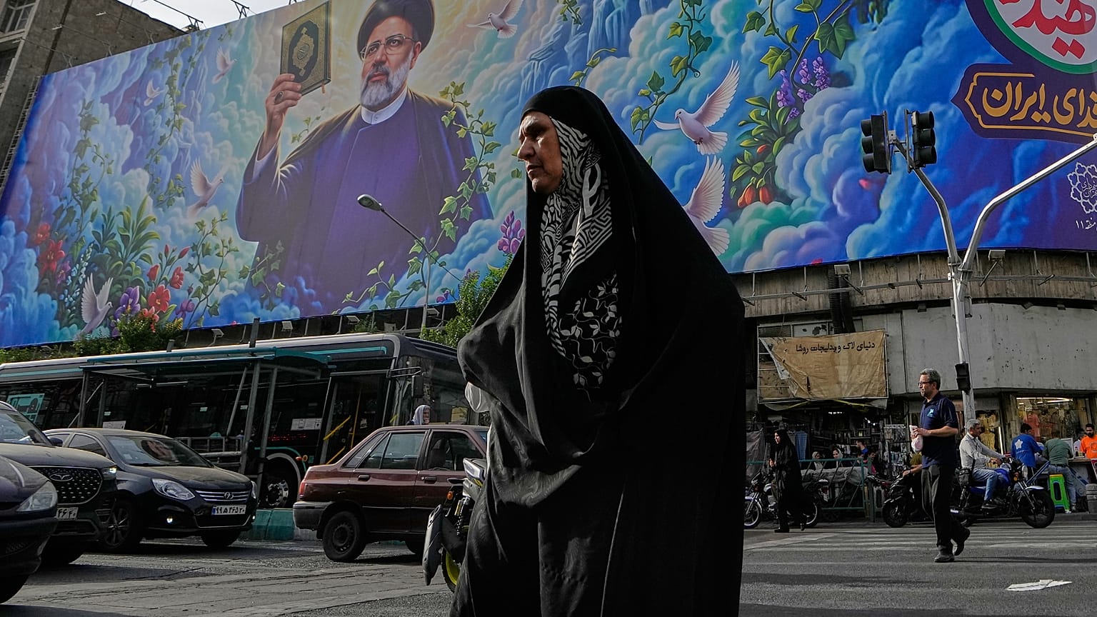 امرأة تعبر تقاطعًا أمام لوحة إعلانية تظهر صورة الرئيس الإيراني الراحل إبراهيم رئيسي، الذي قُتل في حادث تحطم طائرة هليكوبتر عام 2024، في وسط مدينة طهران، إيران، الخميس 28 مايو 