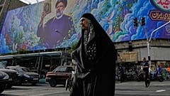 امرأة تعبر تقاطعًا أمام لوحة إعلانية تظهر صورة الرئيس الإيراني الراحل إبراهيم رئيسي، الذي قُتل في حادث تحطم طائرة هليكوبتر عام 2024، في وسط مدينة طهران، إيران، الخميس 28 مايو 