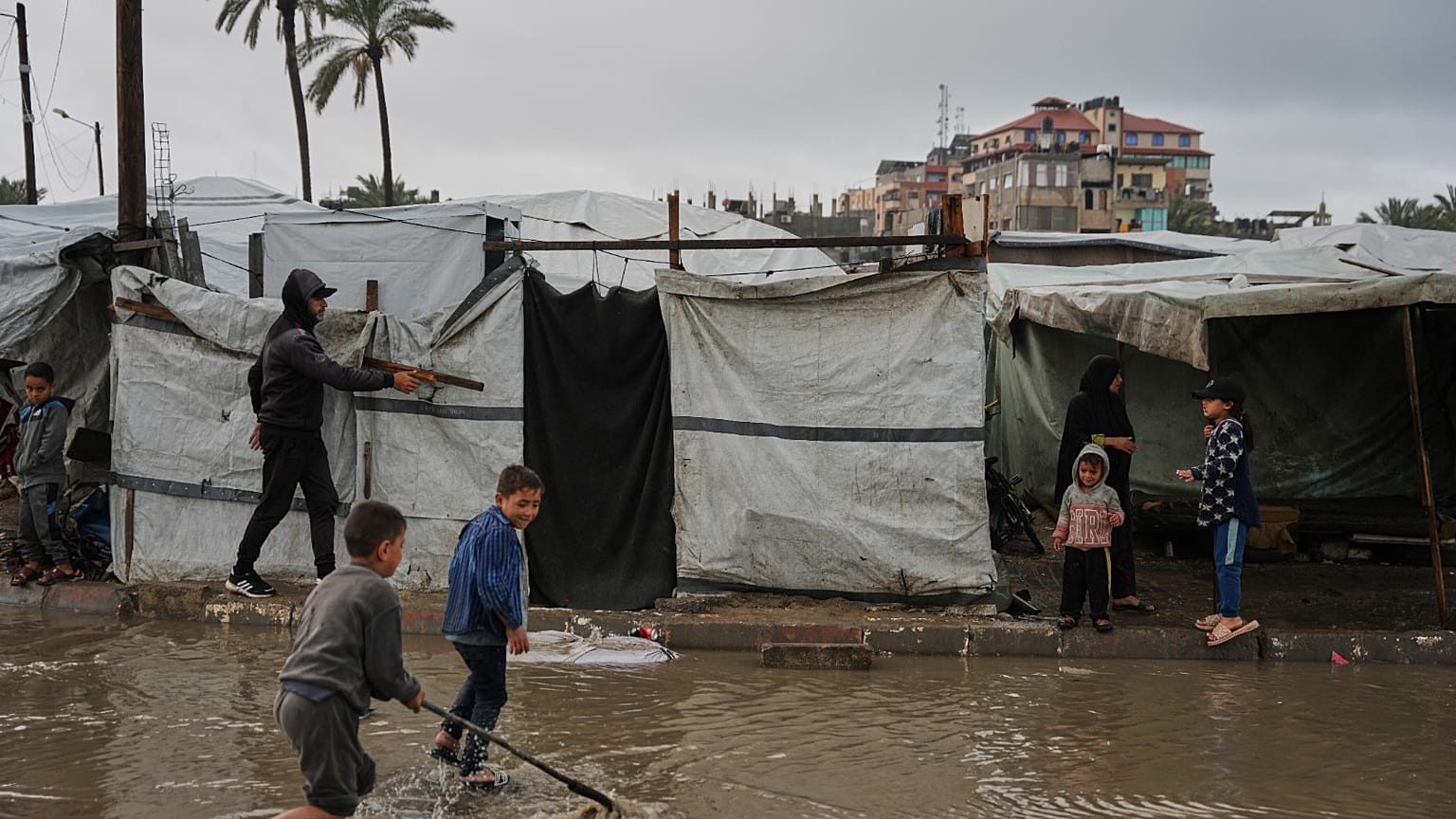 أطفال فلسطينيون نازحون يسيرون عبر مخيم غارق في الأمطار بعد هطول أمطار غزيرة في دير البلح بوسط قطاع غزة، الخميس 26 مارس 2026. 