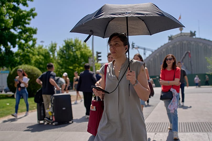 A woman shields herself with an umbrella during a hot day in Madrid, Spain, Wednesday, May 27, 2026. 