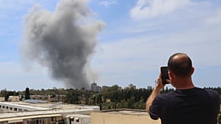 رجل يستخدم هاتفه المحمول لالتقاط الصور بينما يتصاعد الدخان عقب غارة جوية إسرائيلية على مدينة صور الساحلية الجنوبية بلبنان، الأحد 31 مايو 2026