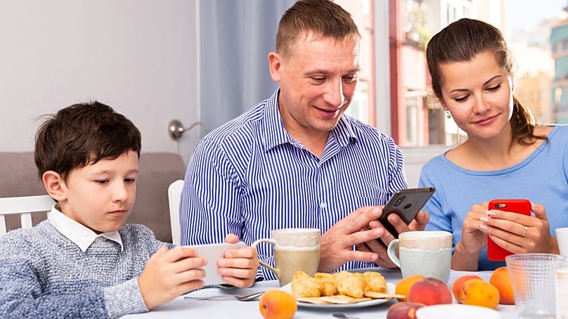عائلة تستخدم الهواتف الذكية أثناء الجلوس إلى مائدة الطعام
