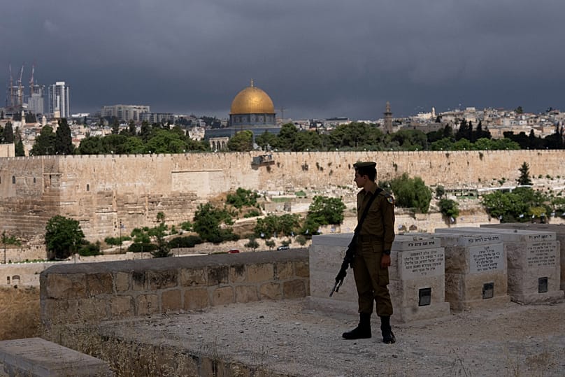 جندي إسرائيلي في مقبرة جبل الزيتون المطلة على البلدة القديمة في القدس، وبخلفه قبة الصخرة في المسجد الأقصى، في 13 مايو 2024.
