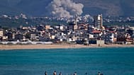 سبح الناس على شاطئ عام بينما يتصاعد الدخان، في الخلفية، من غارة جوية إسرائيلية ضربت قرية القليلة، كما شوهدت من مدينة صور الساحلية الجنوبية بلبنان، الثلاثاء 2 يونيو 2026. 